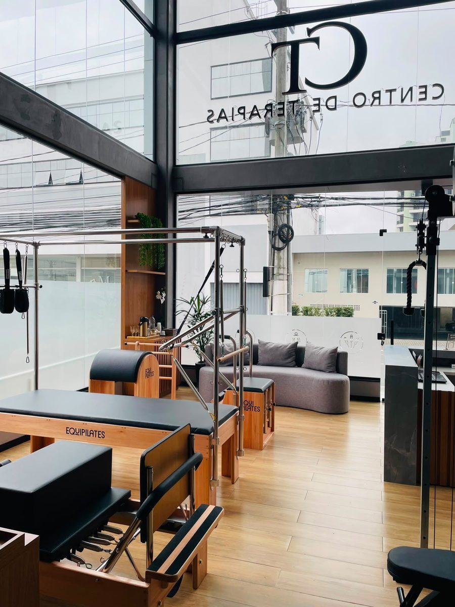 Área de pilates do CT vista pelo vidro, com o sofá da sala de espera ao fundo