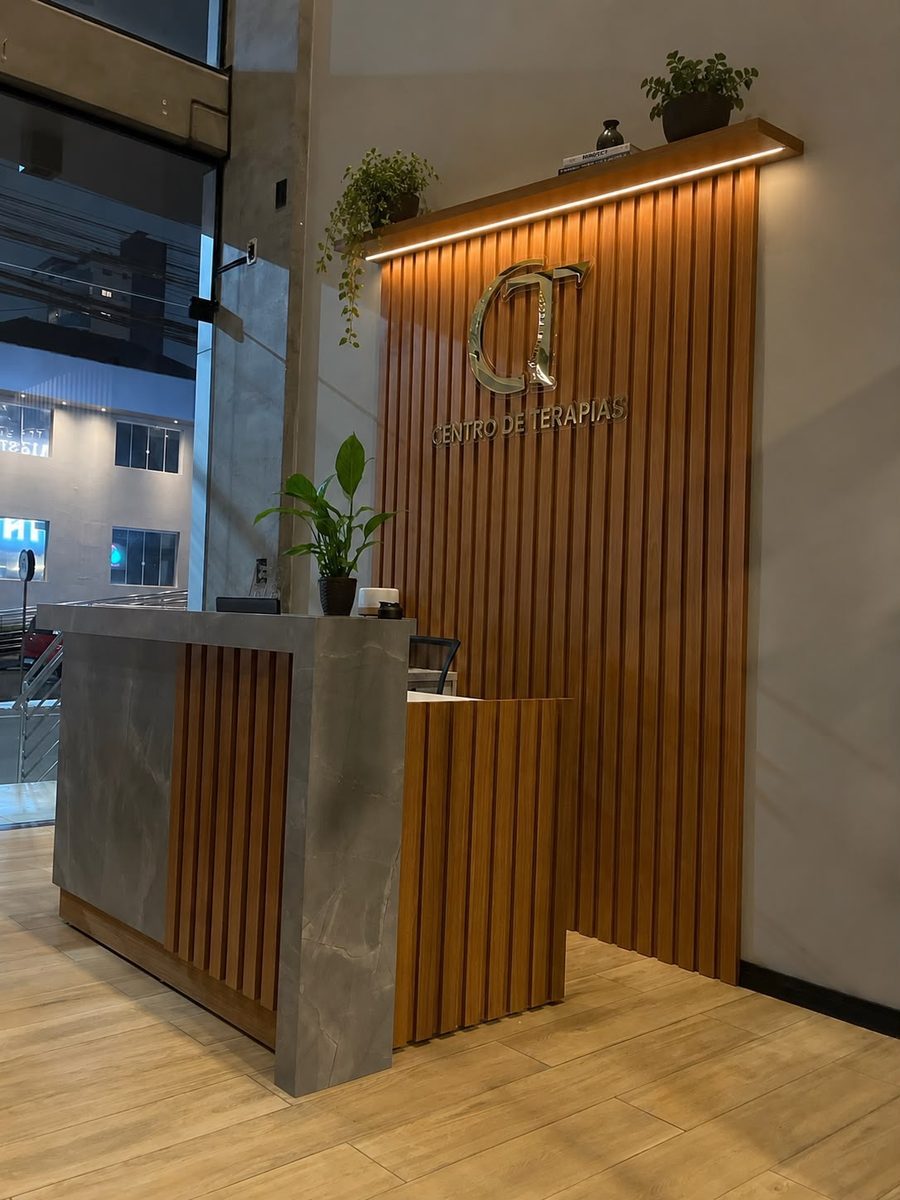 Recepção do CT Centro de Terapias, com balcão e a logo em painel ripado de madeira