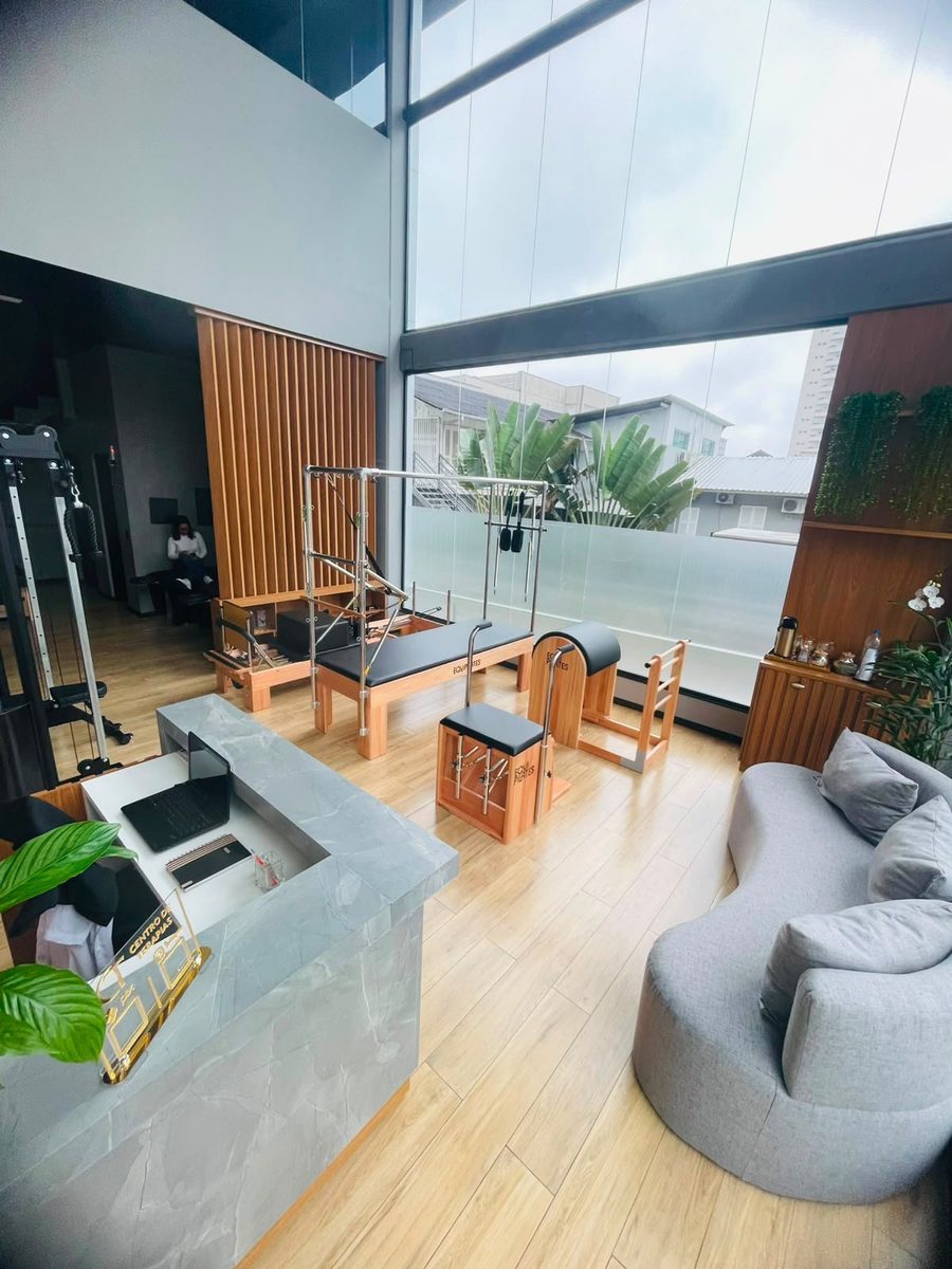 Salão principal do CT, com aparelhos de pilates, janelão de vidro e a sala de espera ao fundo